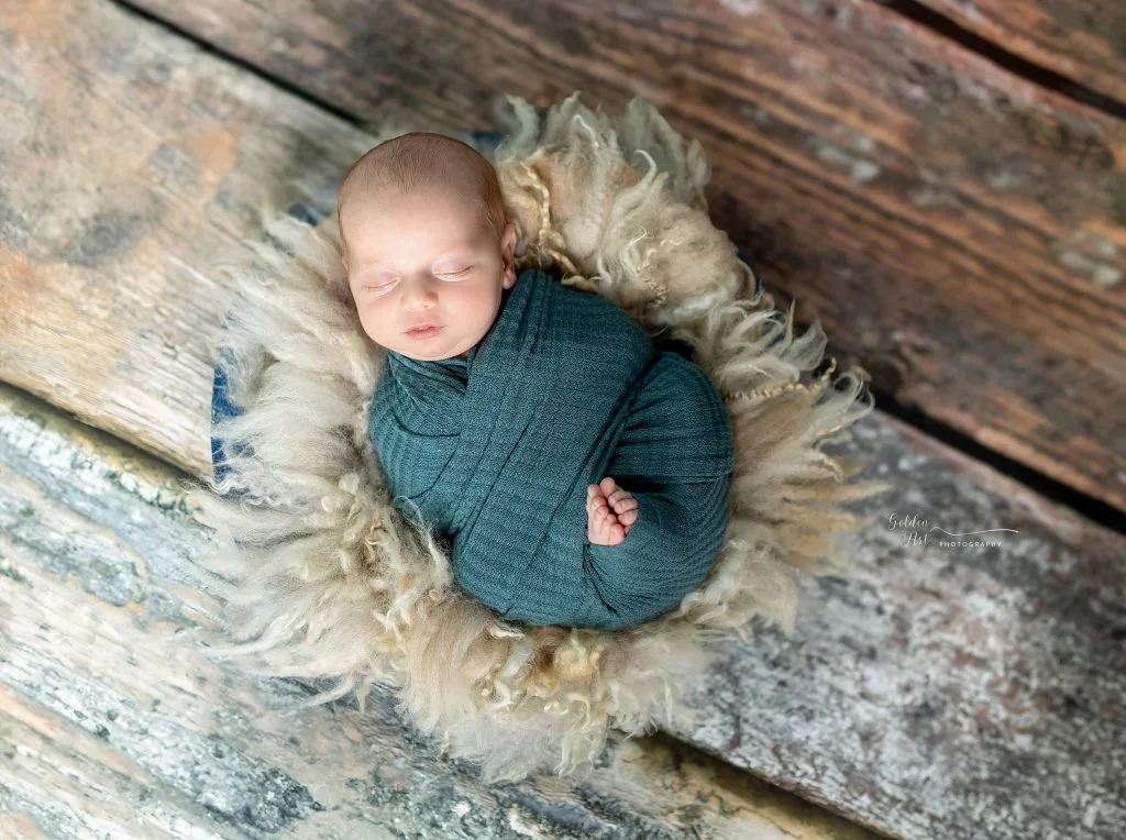 Sleeping newborn wrapped in teal on a textured blanket